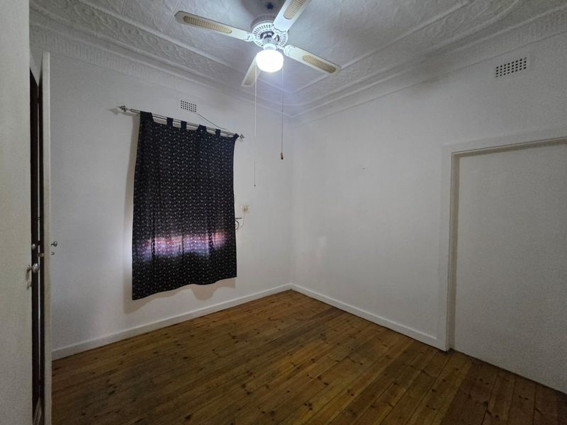 An empty bedroom featuring original timber flooring, a decorative pressed metal ceiling, and a central ceiling fan.