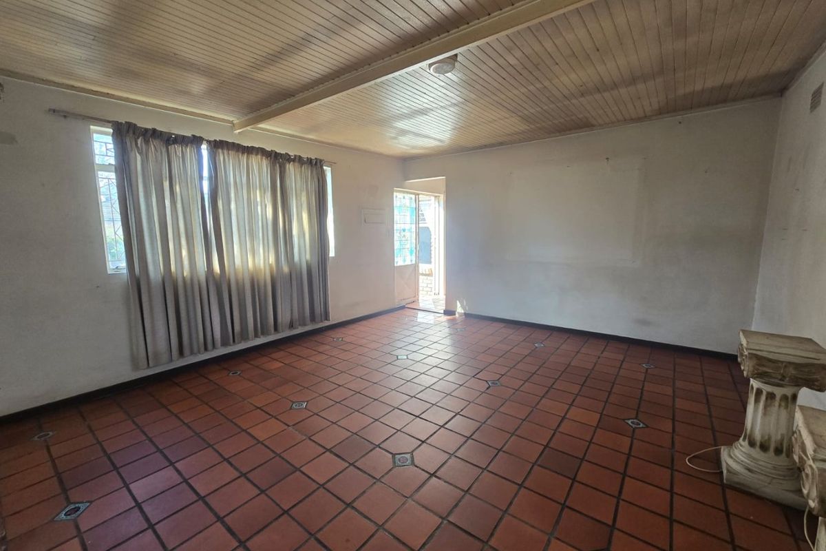 An empty living room featuring traditional terracotta tile flooring and a timber tongue and groove ceiling, offering a blank canvas for renovation.