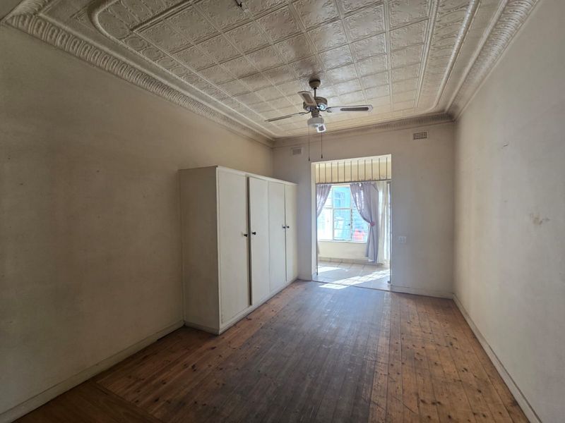 Bedroom featuring original pressed metal ceilings, timber flooring, and a built-in wardrobe, leading to an adjoining sunroom area with security bars.