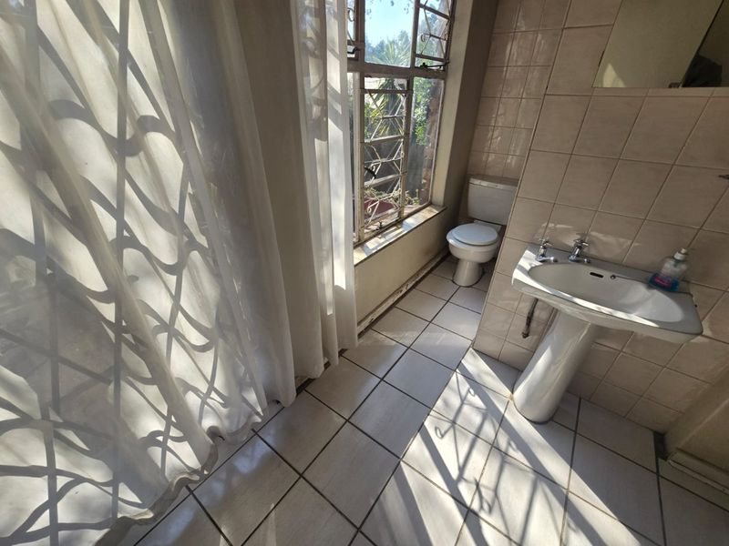 A dated bathroom featuring a pedestal basin, toilet, and tiled finishes, requiring modernization to improve its aesthetic and functionality.
