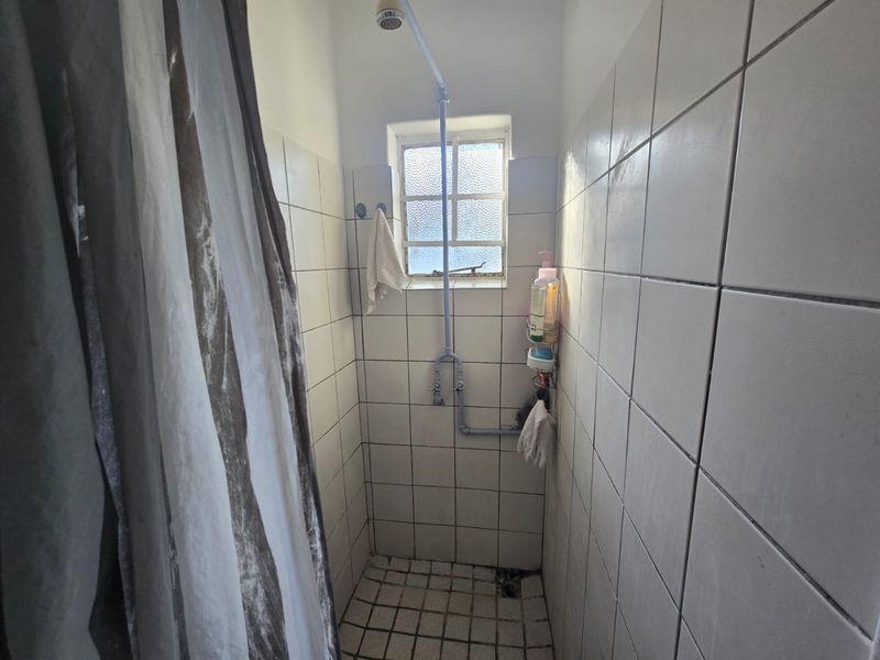 A compact shower enclosure featuring white wall tiles, floor tiling, and exposed surface-mounted plumbing with an obscured glass window.