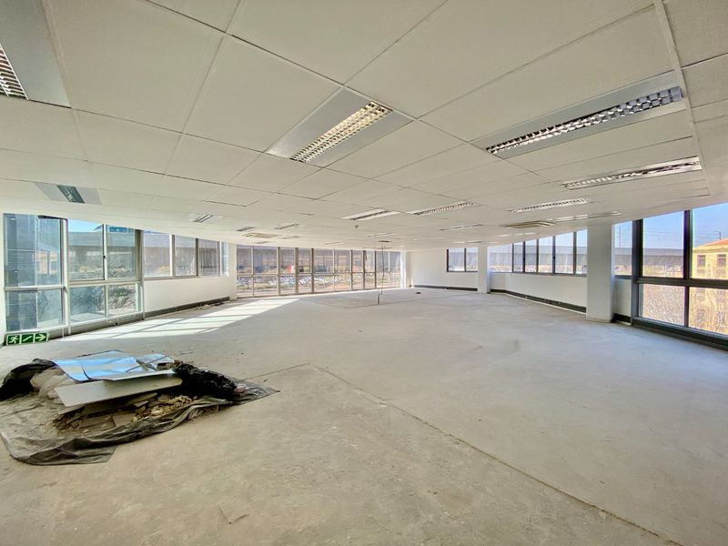 An expansive, open-plan commercial office space featuring a suspended ceiling, recessed lighting, and large windows providing ample natural light, currently in shell condition.