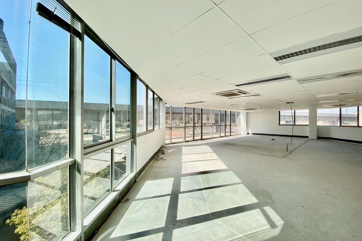 A spacious, vacant commercial office area featuring large floor-to-ceiling windows, suspended ceilings with recessed lighting, and central air conditioning, ready for custom fit-out.