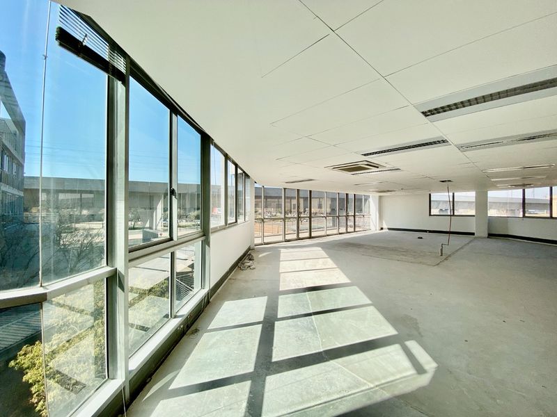 A spacious, vacant commercial office area featuring large floor-to-ceiling windows, suspended ceilings with recessed lighting, and central air conditioning, ready for custom fit-out.