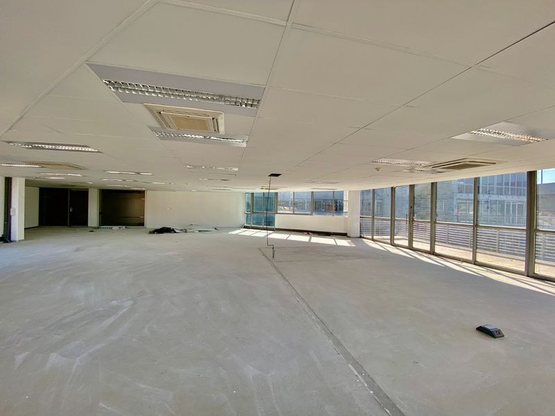 Spacious open-plan commercial office space featuring large windows, suspended ceilings with integrated lighting, and air conditioning units, currently in a shell condition.