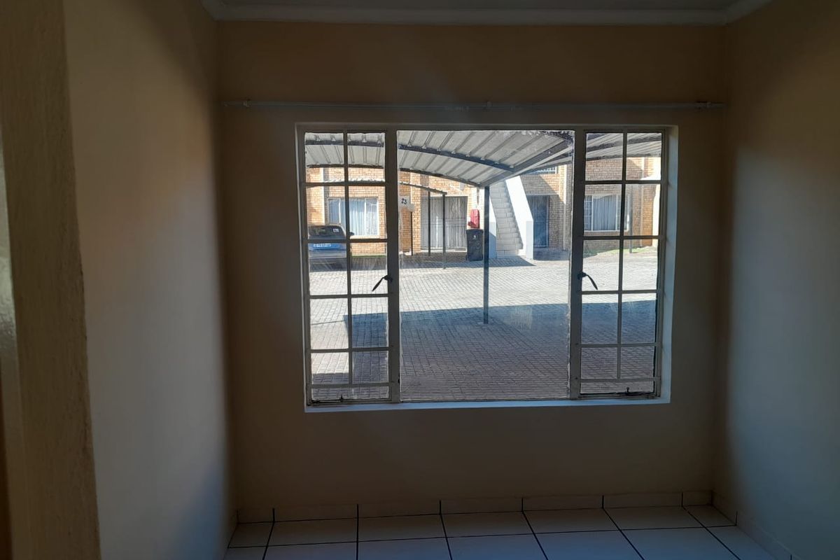 An empty living room featuring tiled flooring and a large window overlooking the exterior parking area.