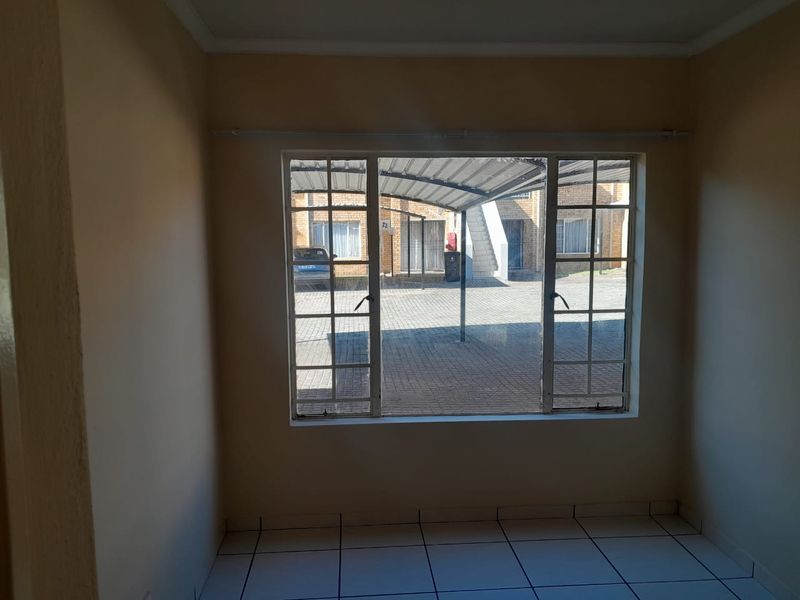 An empty living room featuring tiled flooring and a large window overlooking the exterior parking area.