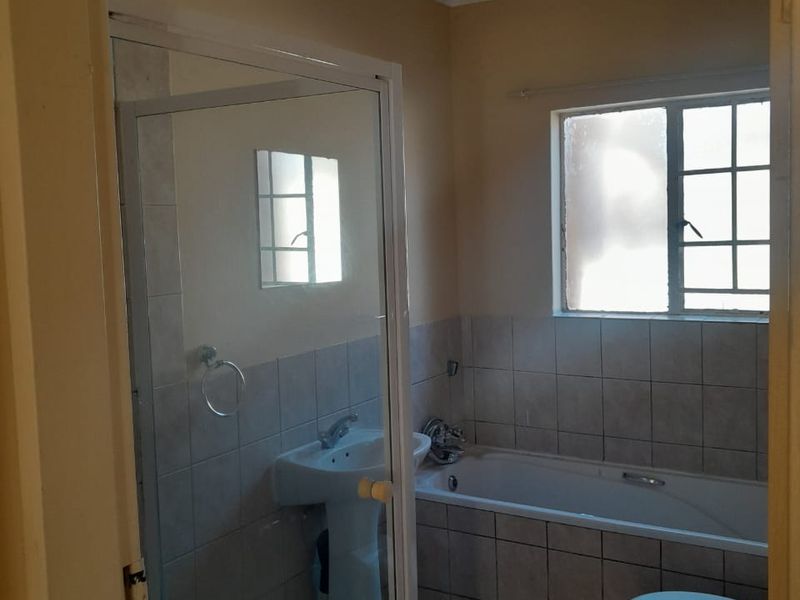 A functional bathroom featuring a shower enclosure, built-in bathtub, and pedestal basin, finished with neutral wall and floor tiling.