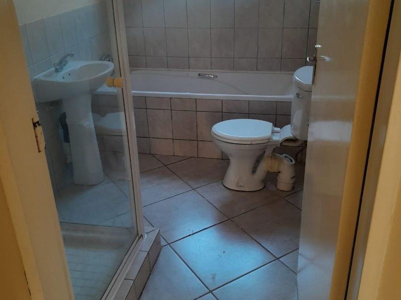 A functional bathroom featuring a pedestal basin, shower enclosure, bathtub, and toilet with tiled finishes throughout.
