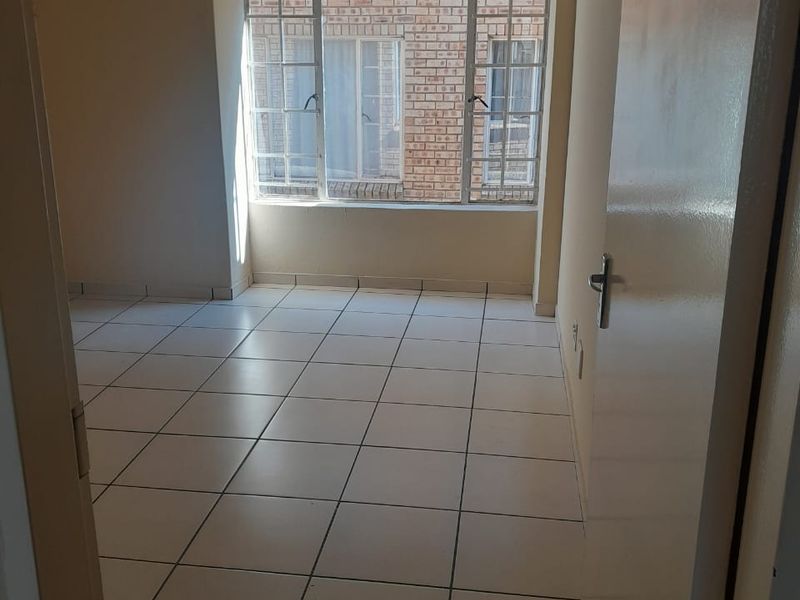 An empty bedroom featuring neutral tiled flooring and large metal-framed windows, providing a blank canvas for potential interior design and furnishing.