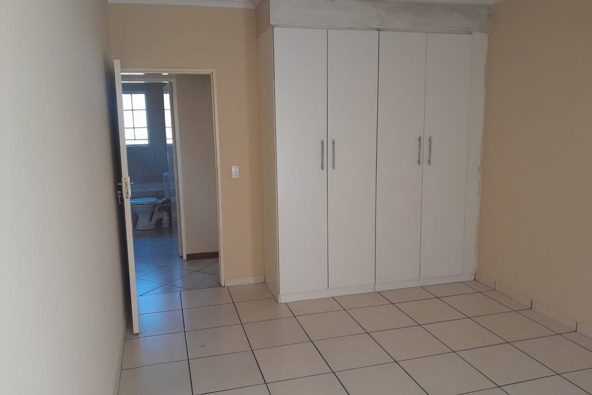An empty bedroom featuring tiled flooring and built-in cupboards, with an adjacent bathroom visible through the doorway.