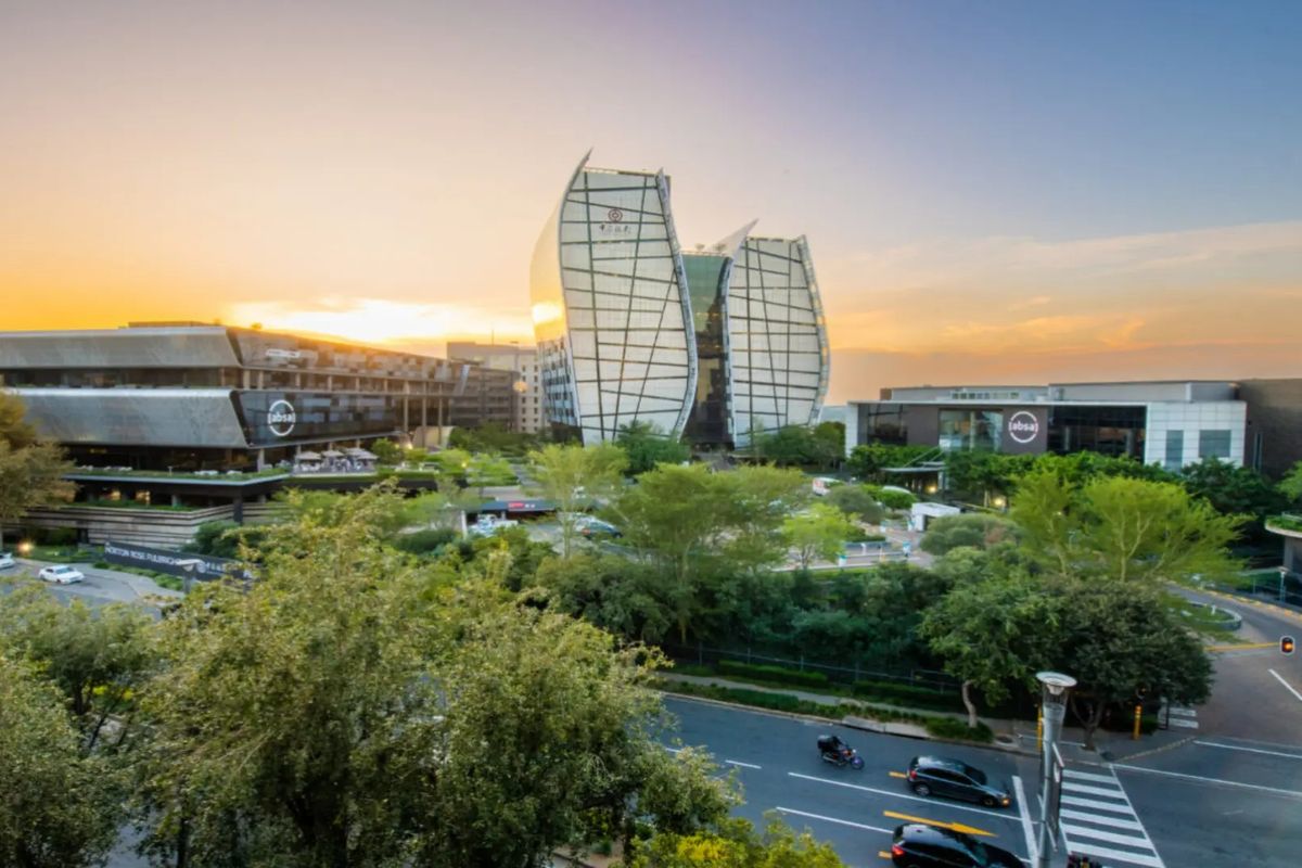 An elevated aerial view of a modern commercial office park featuring contemporary architecture, landscaped green spaces, and surrounding road infrastructure at sunset.