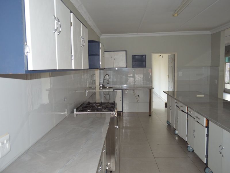 A spacious, empty kitchen featuring stone countertops, a gas hob, built-in oven, and ample fitted cabinetry with tiled flooring and splashbacks.