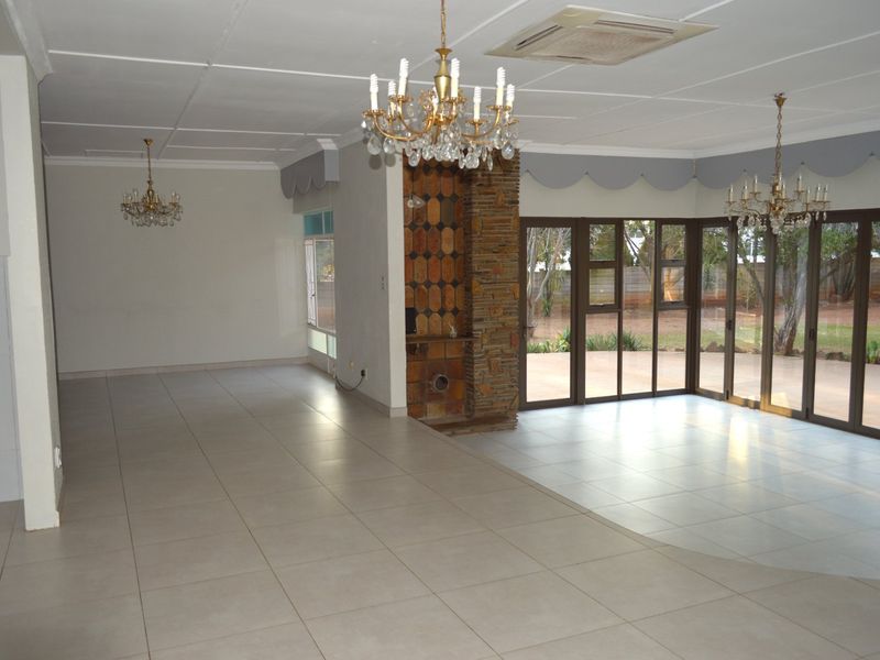 Spacious open-plan living area featuring large aluminium sliding doors, tiled flooring, a central stone fireplace, and integrated ceiling air conditioning.