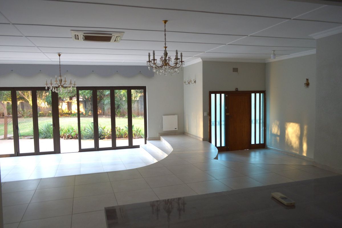 Spacious living area featuring a sunken floor design, large bi-fold glass doors opening to the garden, and elegant crystal chandeliers.