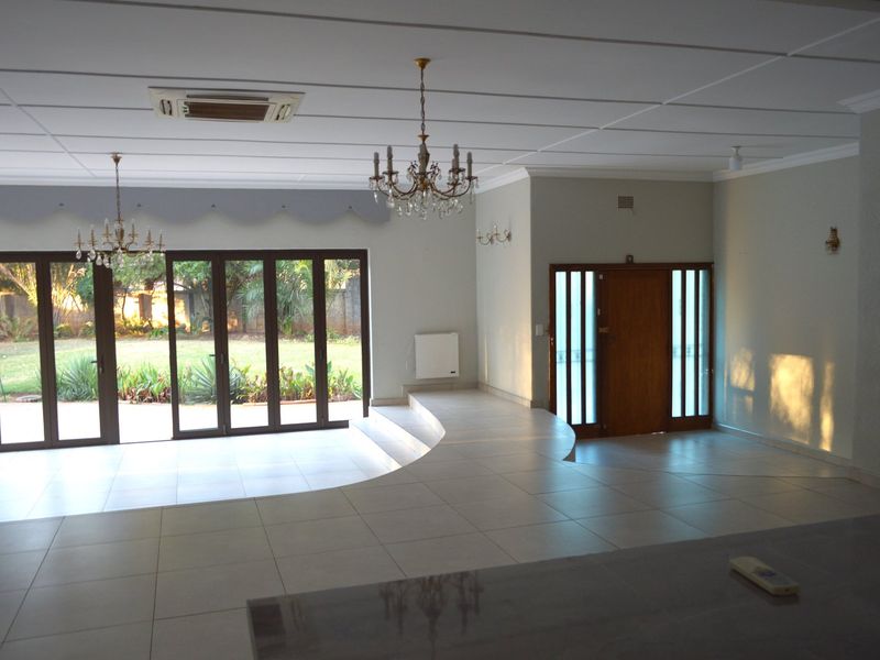 Spacious living area featuring a sunken floor design, large bi-fold glass doors opening to the garden, and elegant crystal chandeliers.