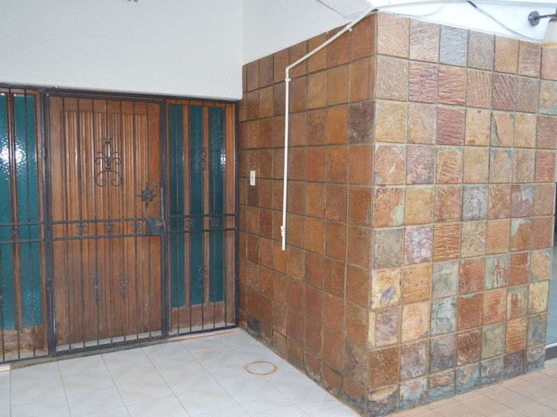 Entrance area featuring a wooden door with security gate, decorative tiled wall cladding, and ceramic floor tiles.