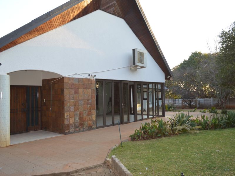Rear view of the house featuring a tiled patio, extensive aluminium sliding doors, and stone cladding accents, overlooking a landscaped garden.
