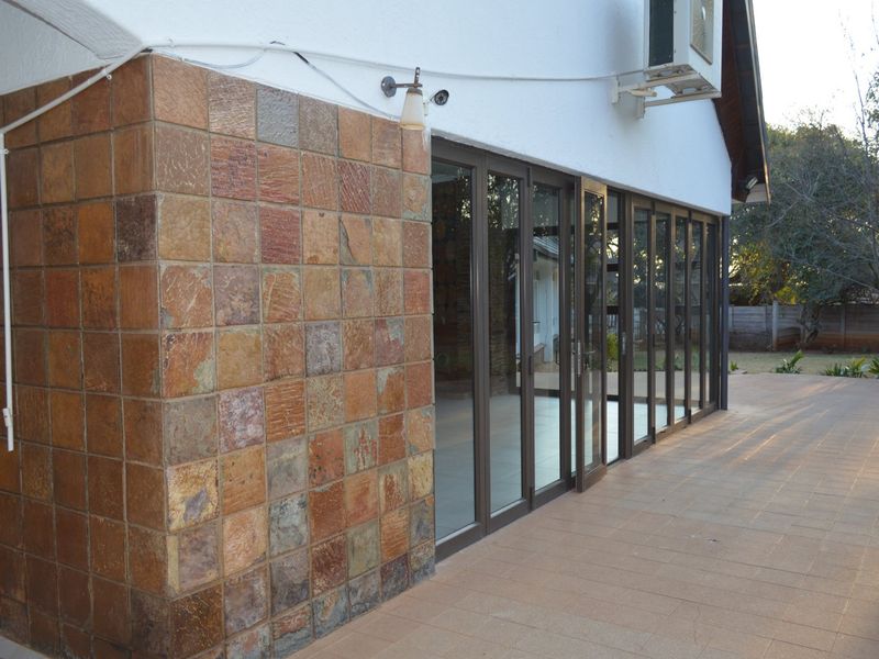 A spacious tiled patio featuring a stone-clad accent wall and large aluminium stacker doors providing seamless access to the interior living space.