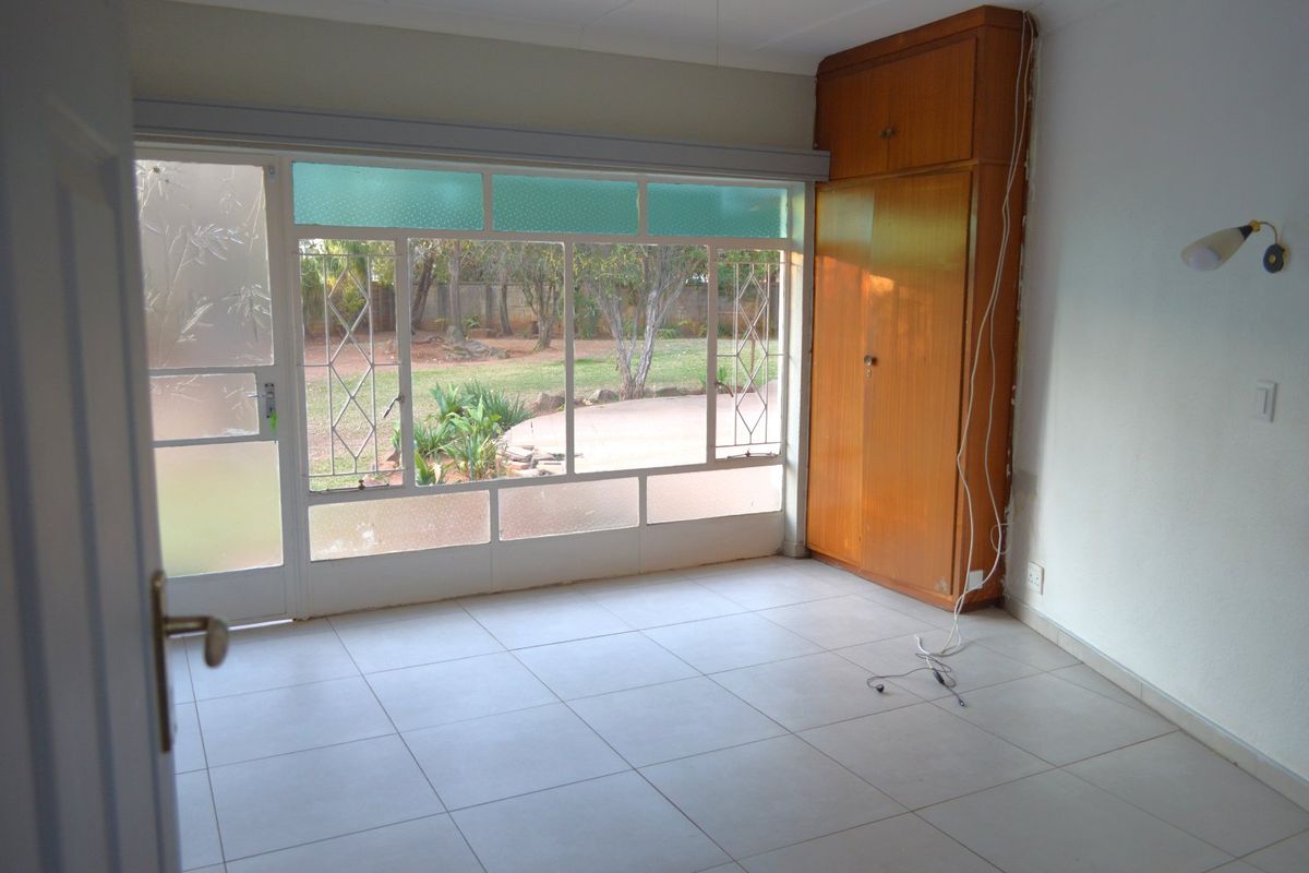 An empty bedroom featuring tiled floors, a built-in wooden wardrobe, and large windows providing natural light and garden views.