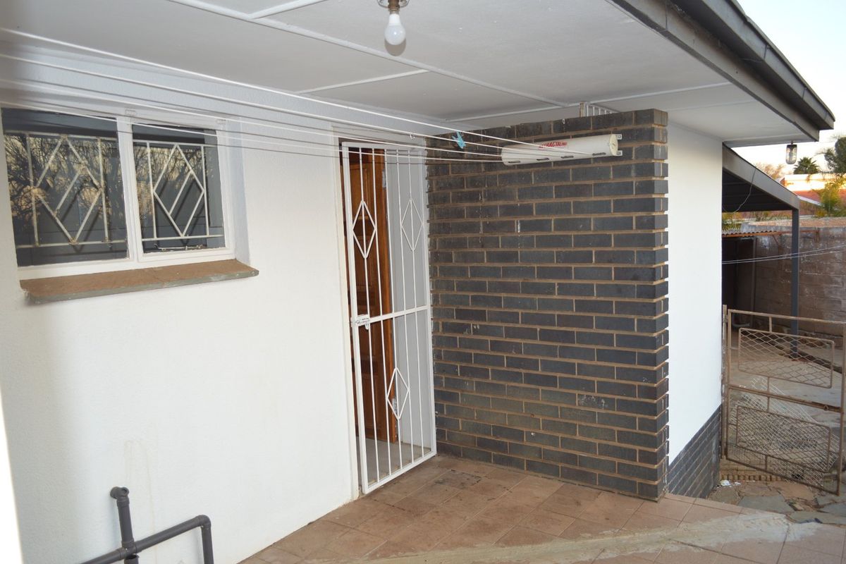 A covered rear patio area featuring a brick accent wall, security gate, and a retractable clothesline, providing functional outdoor utility space.