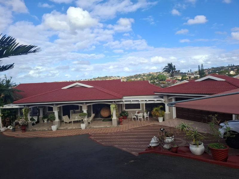 A well-maintained single-story house featuring a red tiled roof, a spacious covered patio, and an expansive paved driveway leading to the garage.