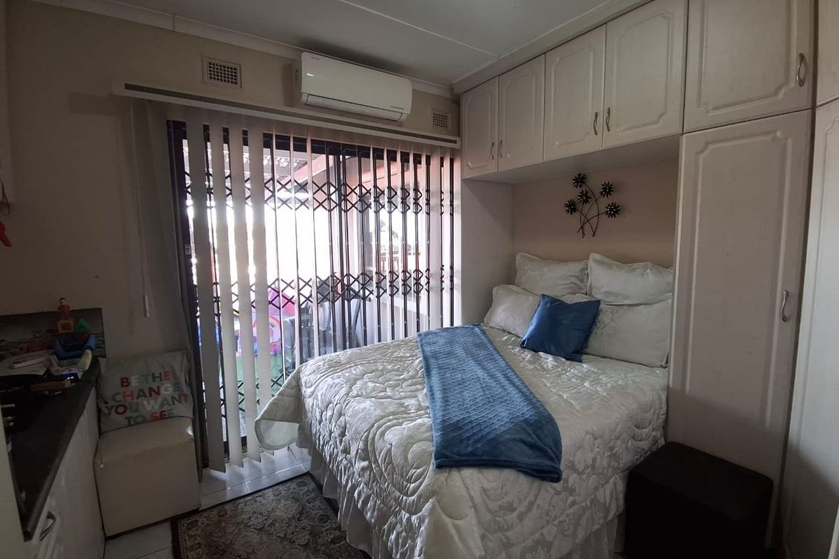 A compact bedroom featuring built-in cabinetry, a split-system air conditioner, and direct access to an outdoor area through a sliding glass door.