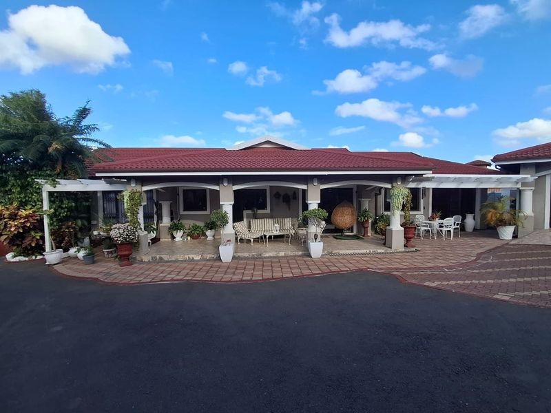 A well-maintained front elevation featuring a spacious covered patio, decorative columns, a tiled roof, and a paved driveway area.