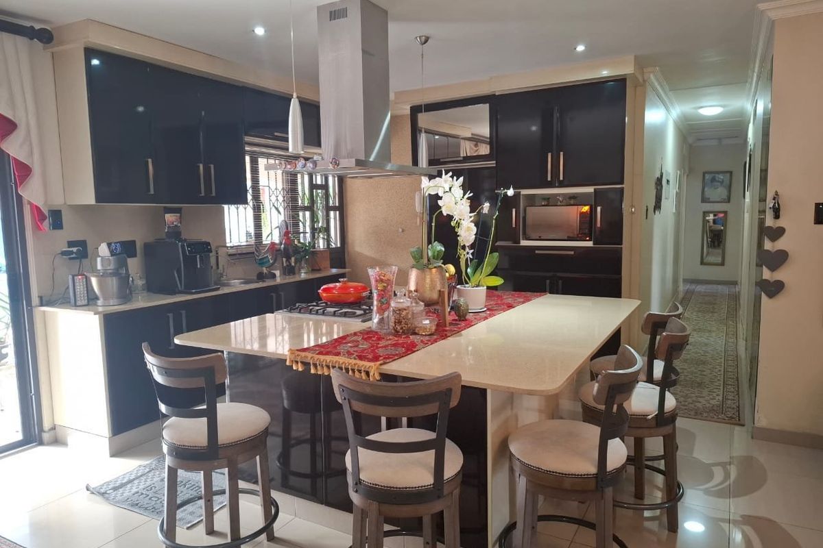 Modern kitchen featuring high-gloss black cabinetry, a large central island with stone countertop, integrated appliances, and recessed lighting, flowing into a hallway.