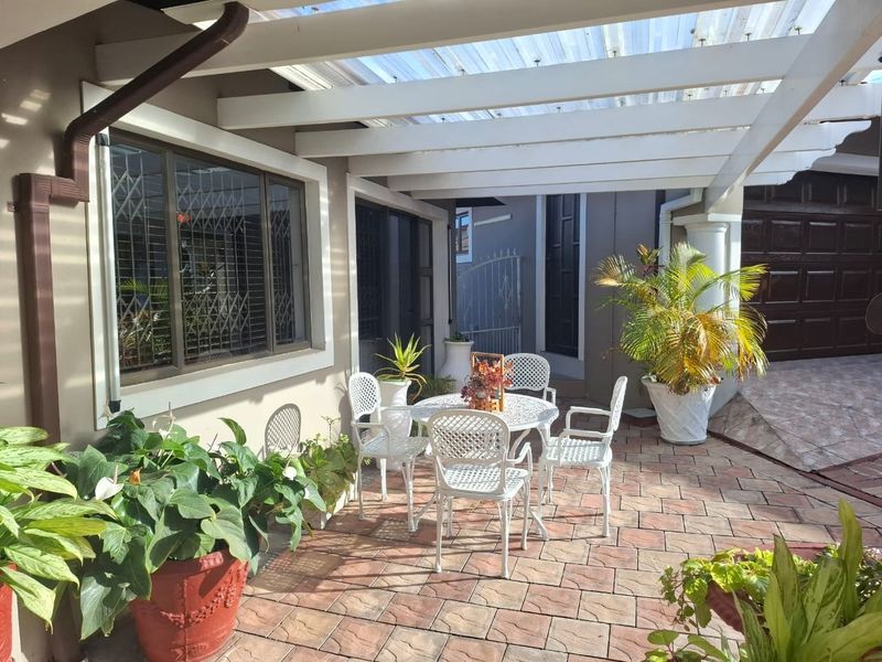 A covered outdoor patio area featuring paved flooring, a pergola structure with translucent roofing, and secure window treatments.