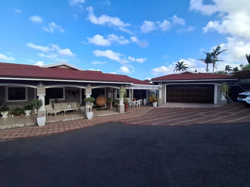Front view of a well-maintained house featuring a covered patio, tiled roof, and a spacious paved driveway leading to a double garage.