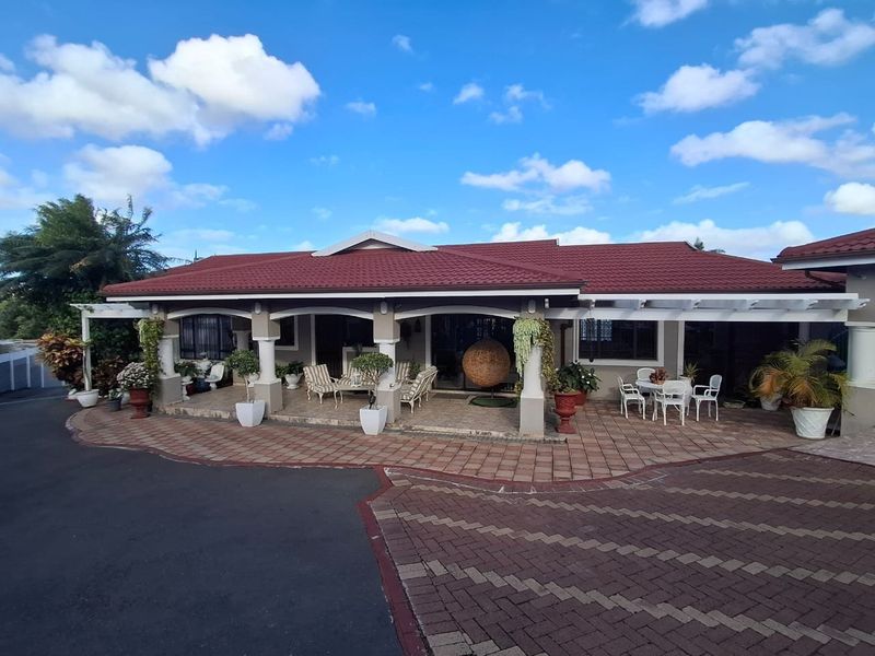 A spacious covered patio area featuring tiled flooring and concrete columns, providing an inviting outdoor entertainment space overlooking the paved driveway.