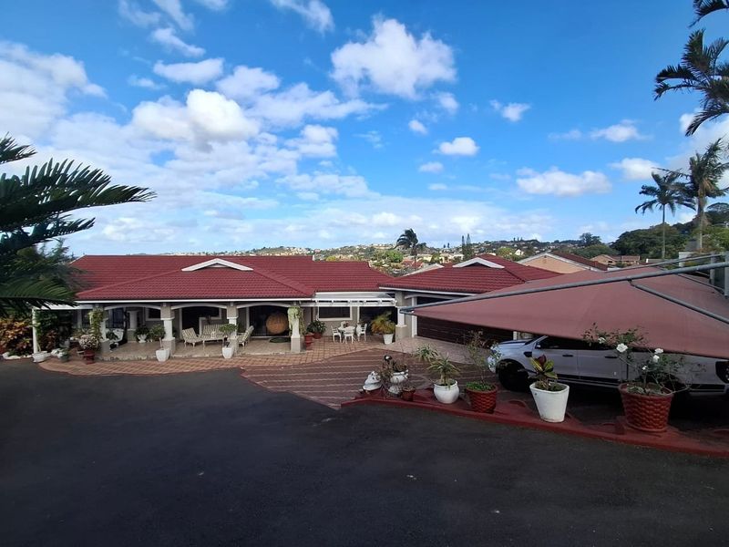 Front elevation of a single-story house featuring a tiled roof, covered patio area, paved driveway, and a shade sail carport.