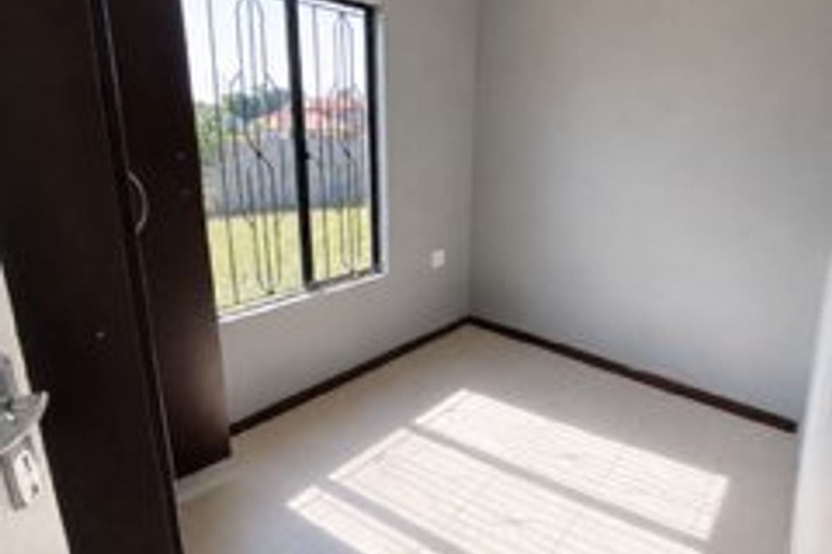 A clean, empty bedroom featuring neutral grey walls, tiled flooring, and a built-in wardrobe with security bars on the window.