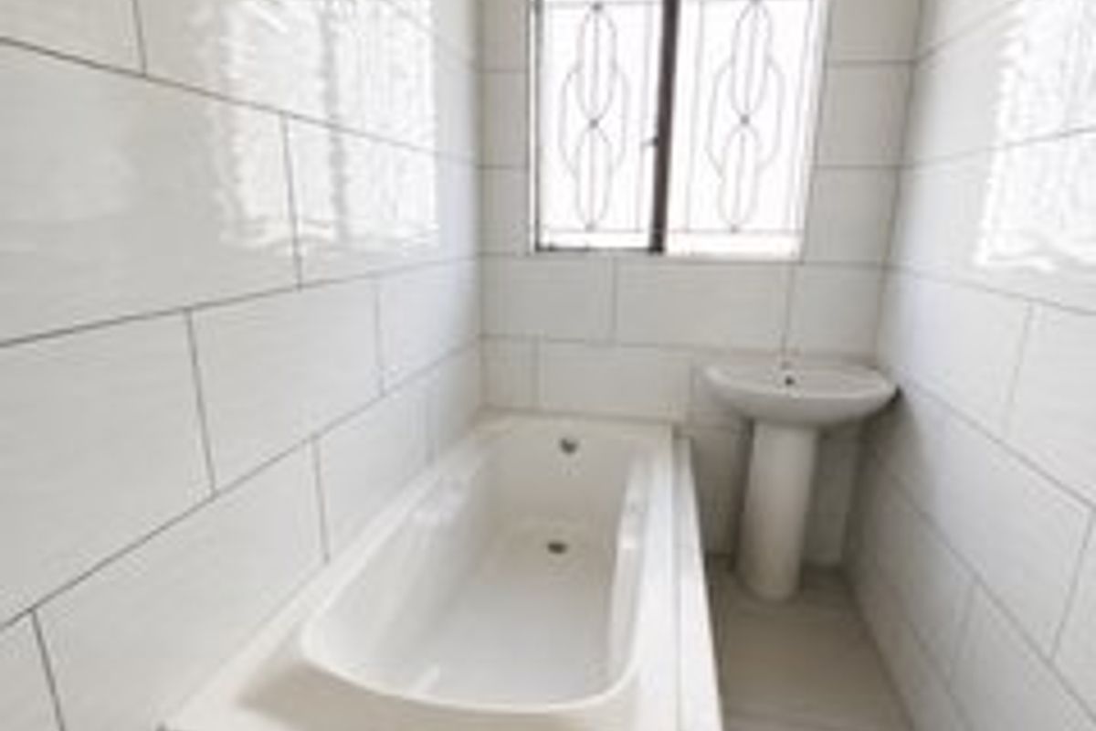 A clean, minimalist bathroom featuring a built-in bathtub, pedestal basin, and full-height wall tiling with a secure window.