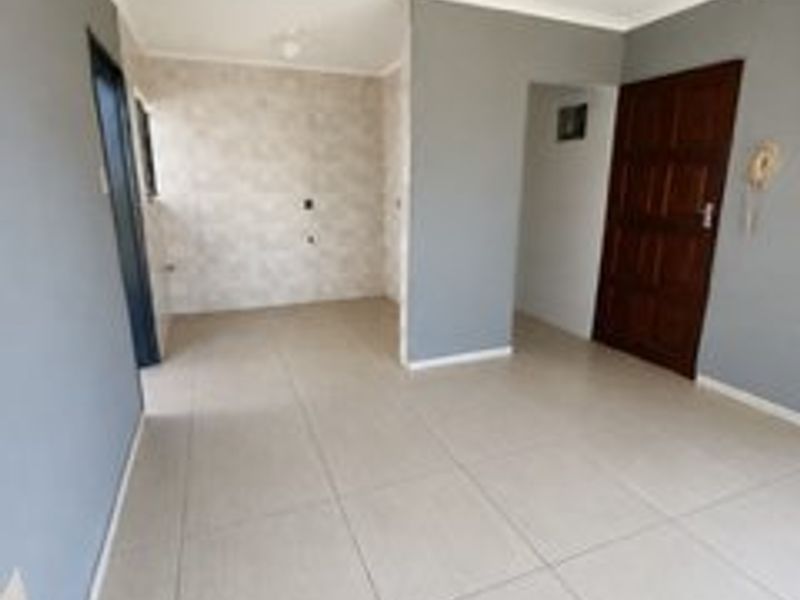 An empty open-plan living area featuring neutral tiled flooring, grey painted walls, and coved cornicing, providing a versatile space for interior design.