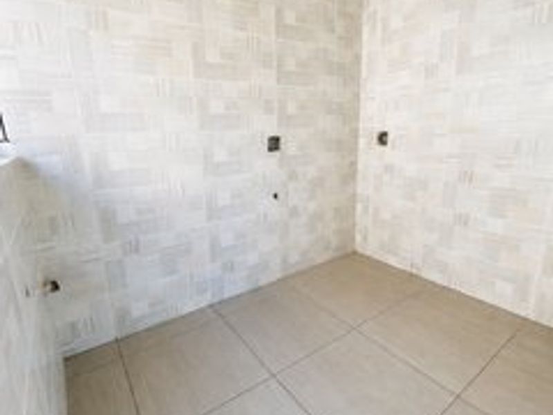 A clean, empty laundry area featuring neutral wall and floor tiling with existing plumbing and electrical connections ready for appliance installation.
