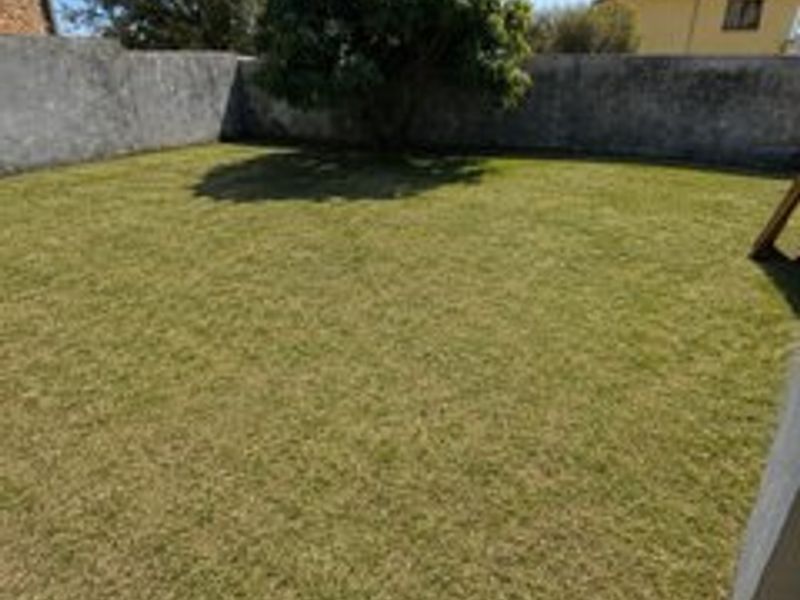 A private rear garden featuring a well-maintained lawn enclosed by solid boundary walls.