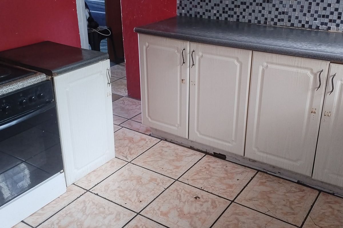 A functional kitchen featuring built-in cabinetry, a mosaic tile backsplash, and tiled flooring, currently showing signs of wear and requiring cosmetic updates.
