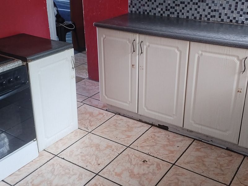 A functional kitchen featuring built-in cabinetry, a mosaic tile backsplash, and tiled flooring, currently showing signs of wear and requiring cosmetic updates.
