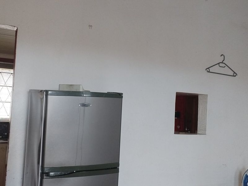 A kitchen area featuring a mosaic tile backsplash, laminate countertops, and security bars on the window, showing signs of wear on the walls.