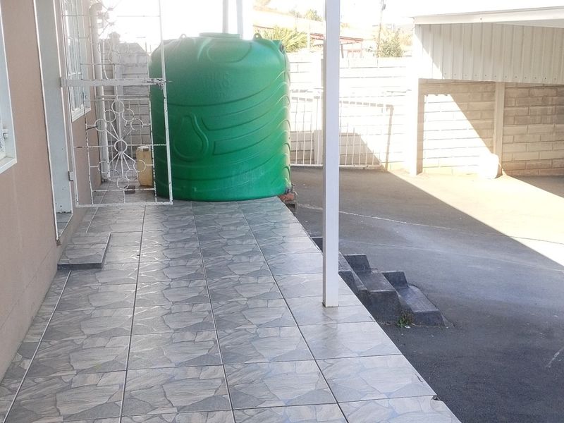 A paved rear patio area featuring a water storage tank, covered carport, and secure boundary walling.