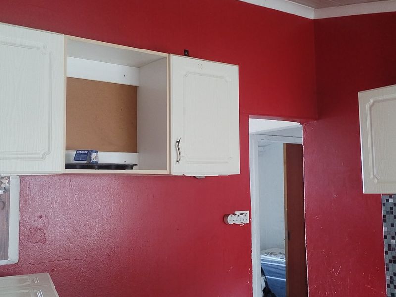 A kitchen area featuring white upper cabinetry, a mosaic tile backsplash, and bold red walls, currently requiring cosmetic updates and repairs.