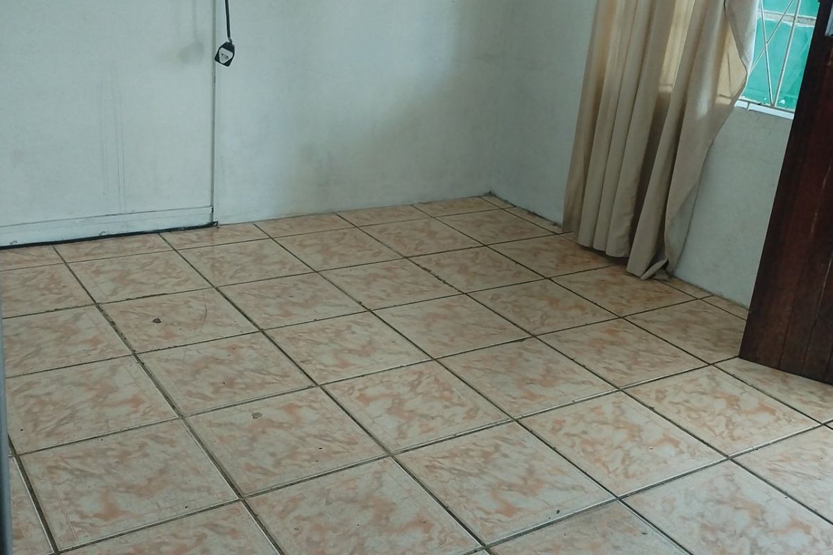 An empty living area featuring ceramic floor tiles, a timber door, and a window with security bars.