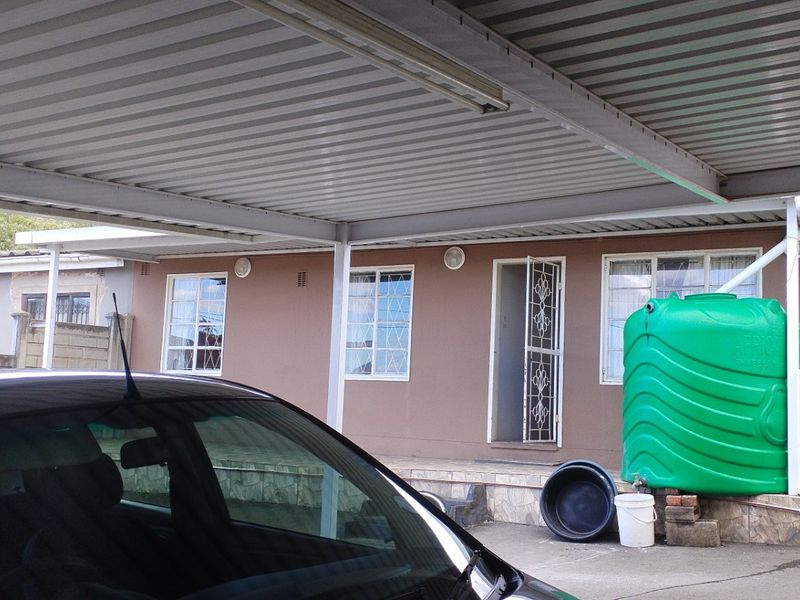 Front exterior view of the house featuring a large corrugated metal carport, a water storage tank, and security features on windows and doors.