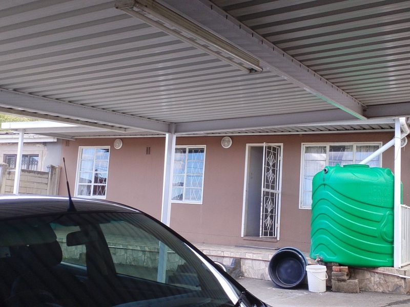 Front exterior view of the property featuring a covered carport, security gates, and a large water storage tank.