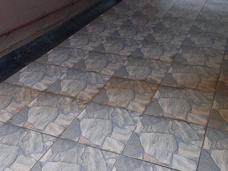 An outdoor patio area featuring stone-look tiled flooring, showing signs of wear and surface staining along the adjacent wall structure.