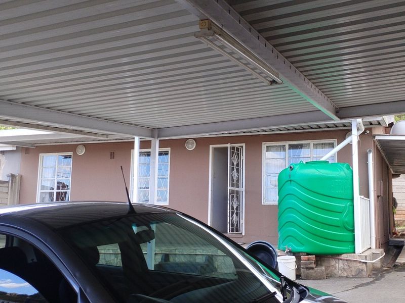 Rear exterior view featuring a large corrugated metal carport, paved driveway, and a green water storage tank attached to the building.