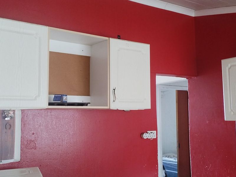 A kitchen area featuring white upper cabinetry and a mosaic tile backsplash, currently requiring cosmetic updates and repairs to the wall and cabinetry.