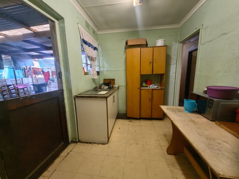 A functional scullery area featuring a stainless steel sink, built-in cabinetry, and tiled flooring, requiring cosmetic updates to improve its overall condition.